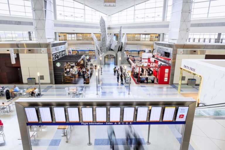 DFW Terminal D concourse with a Starbucks counter, seating, flight information boards, and airport retail.