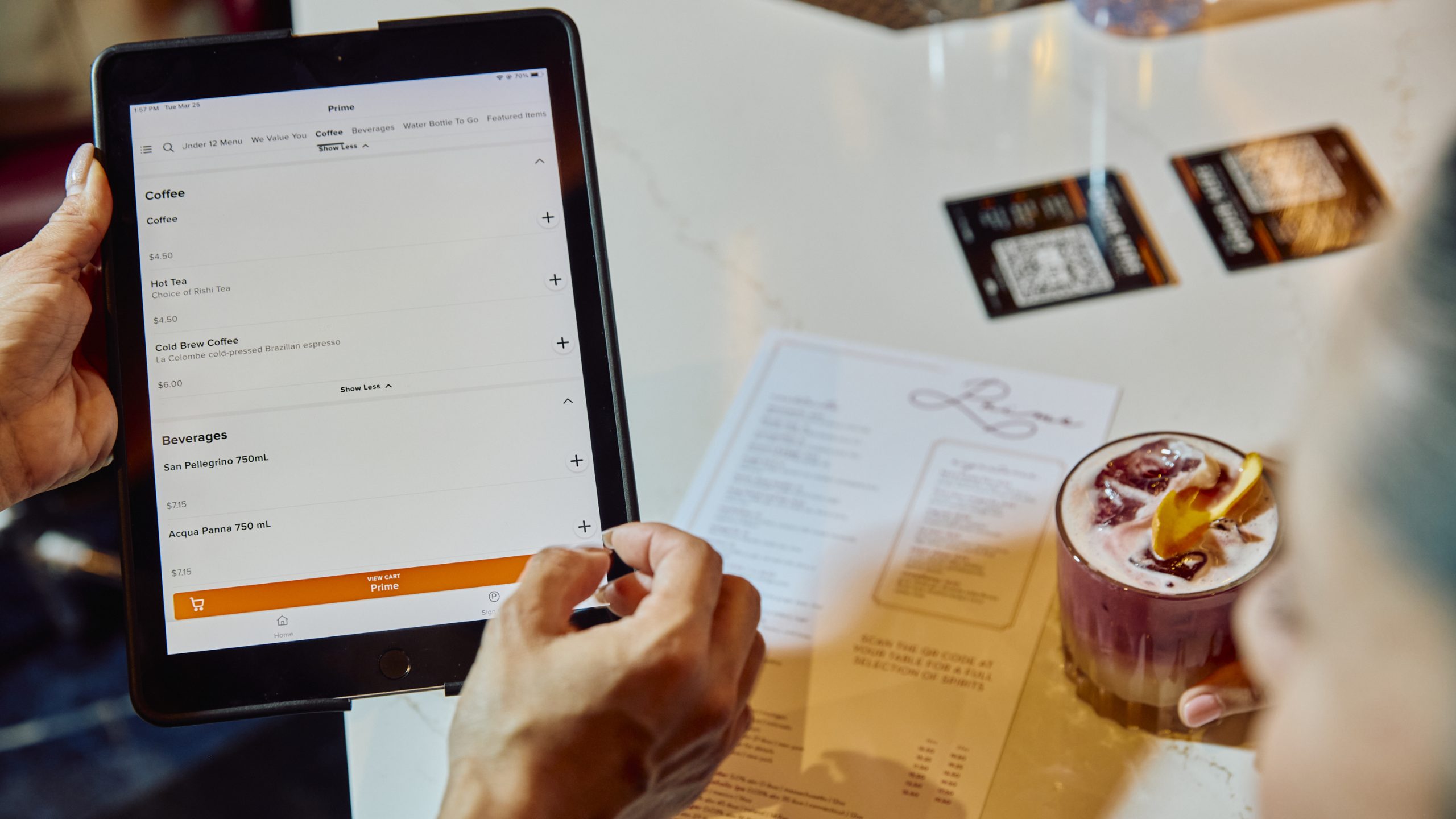 Person using an airport restaurant ordering tablet beside a printed menu and drink. Vegan airport guide.