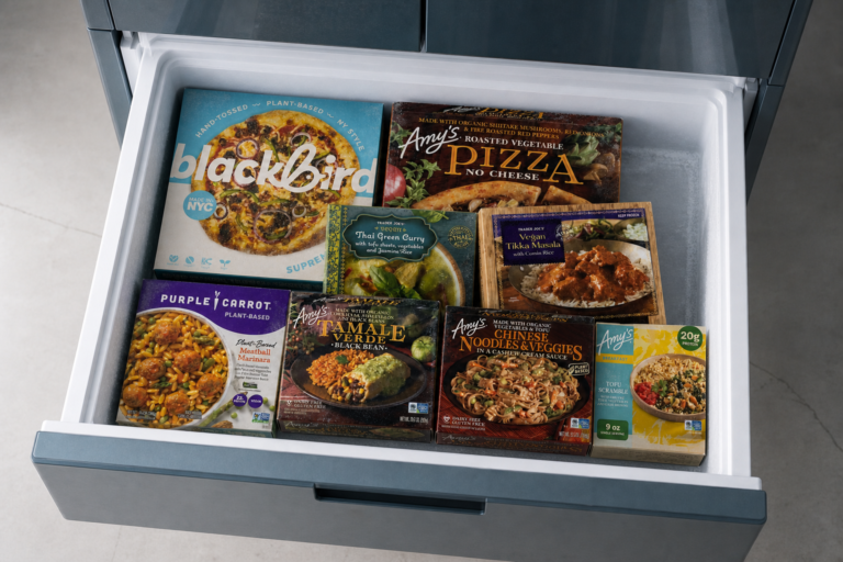 Eight branded vegan frozen dinners stored together inside an open home freezer drawer.