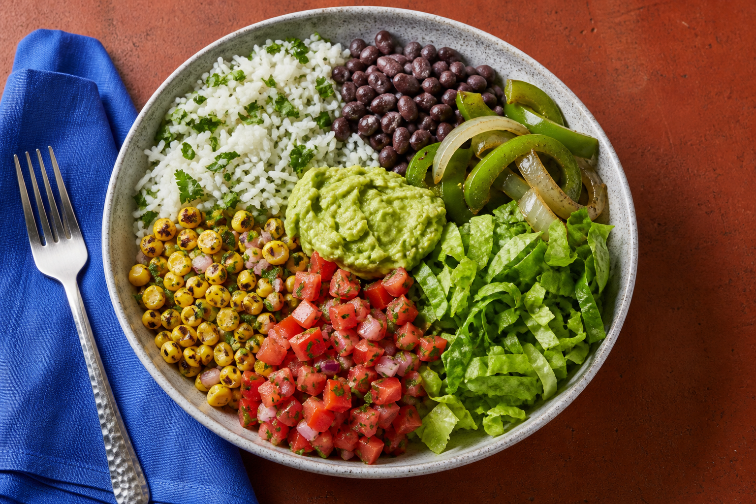 Overhead vegan burrito bowl with rice, black beans, peppers and onions, corn salsa, tomato salsa, guacamole, and lettuce.
