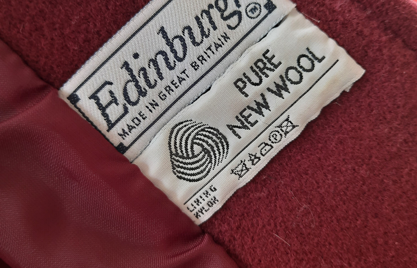 Close view of a secondhand coat label reading Pure New Wool, with the maker label and care symbols visible.