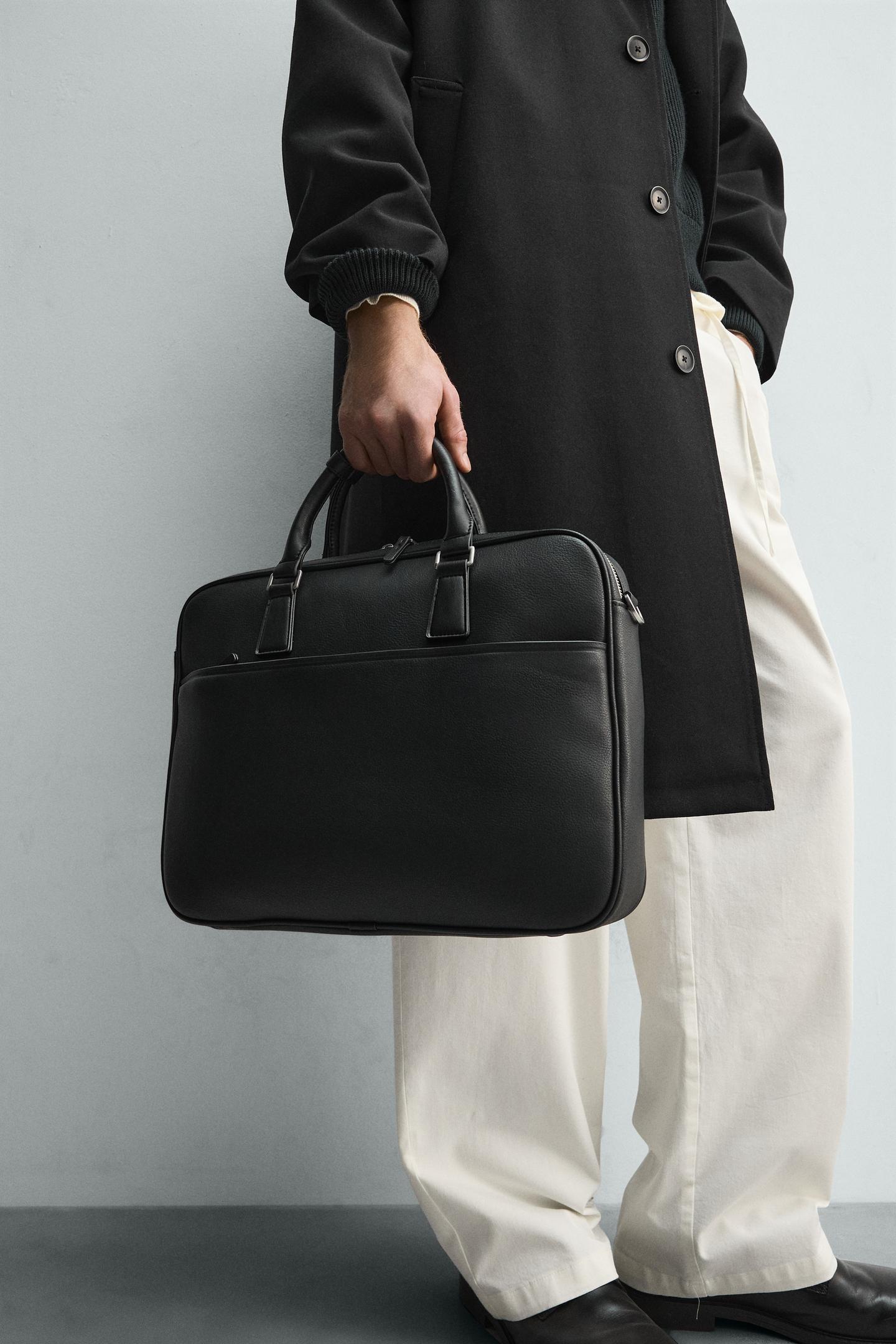 A person carries a black Zara Textured Briefcase by its two handles.